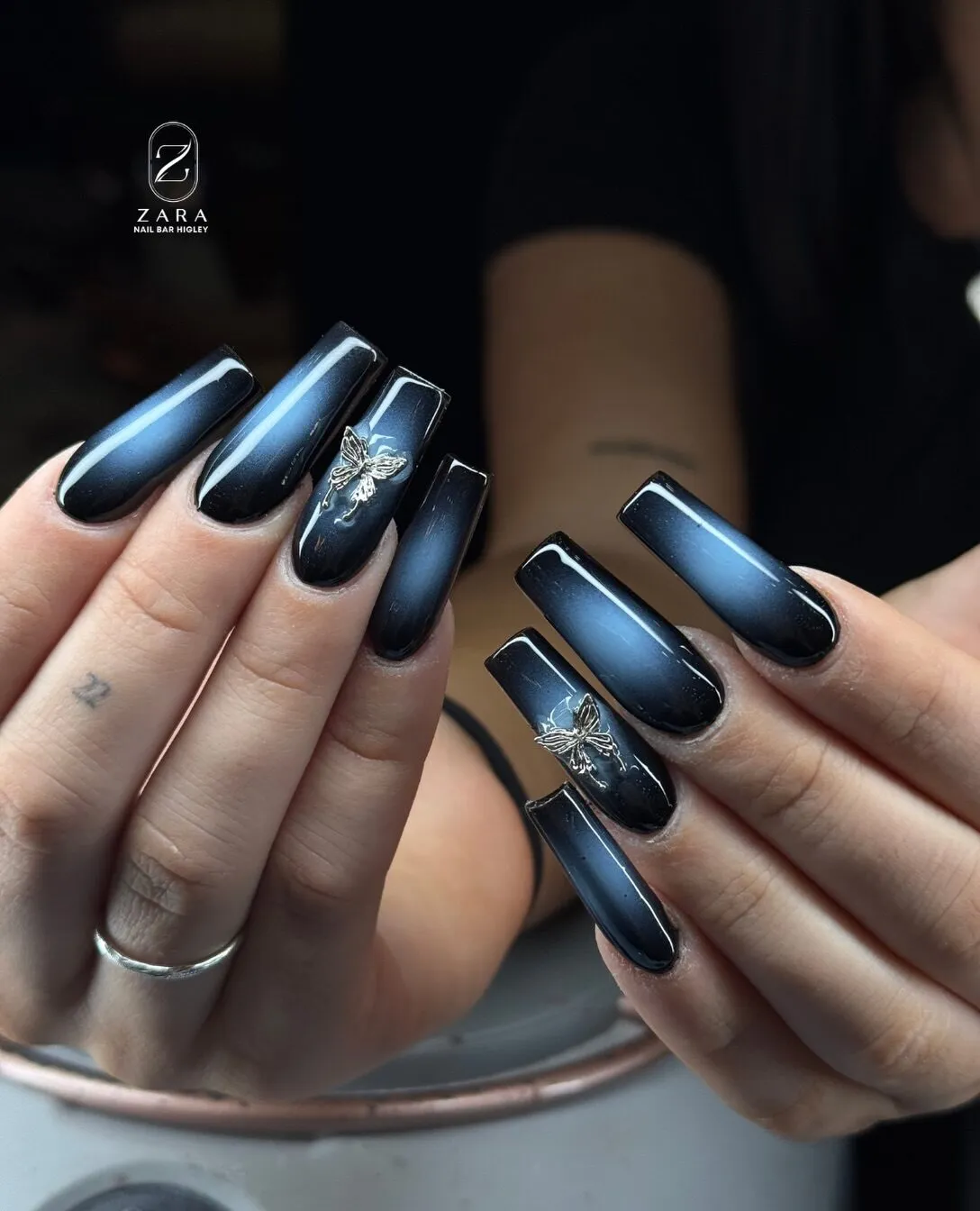 Long square nails in a smoky blue aura over black with silver butterfly charms.
