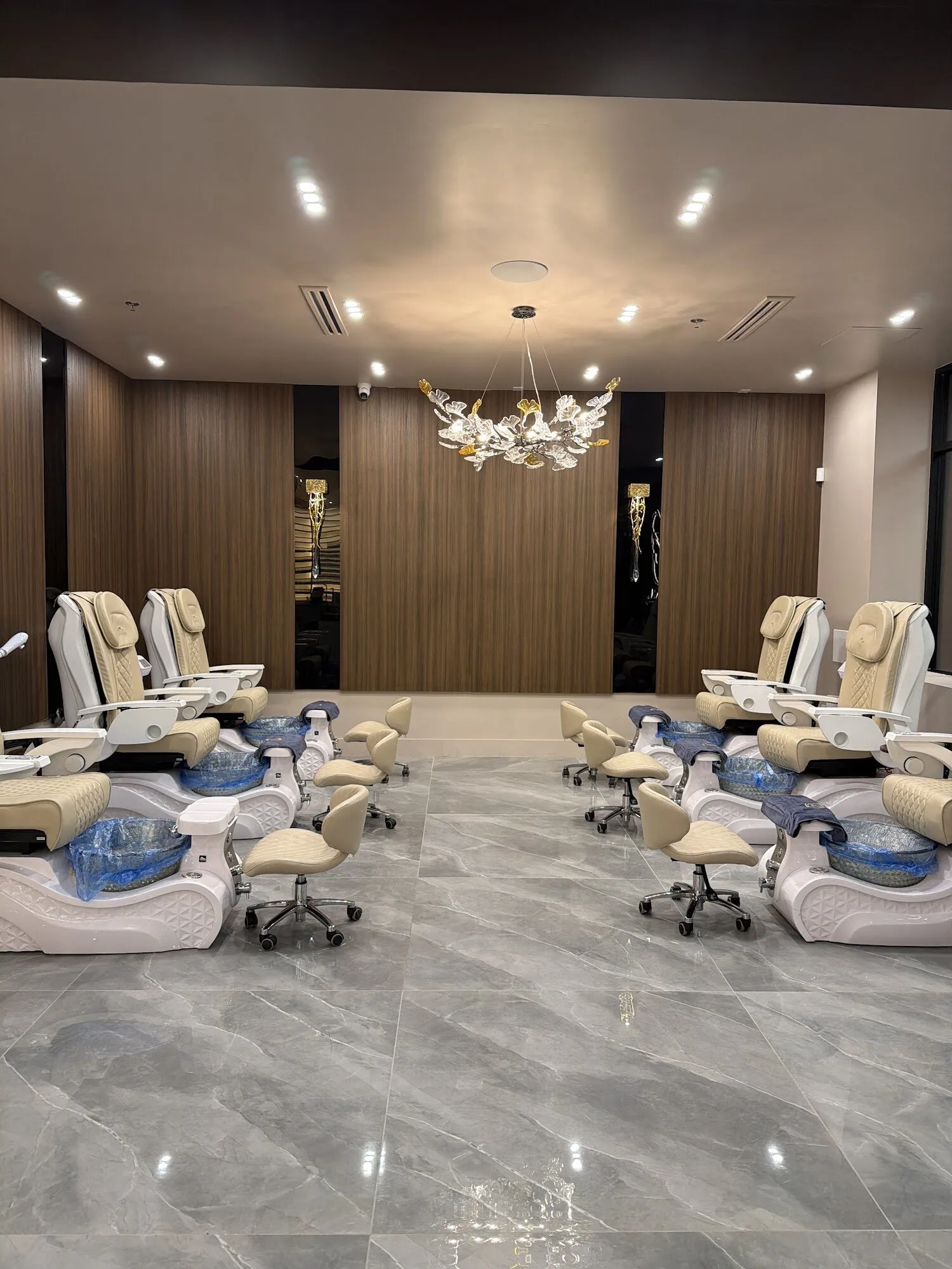 The pedicure lounge at Zara Nail Bar Vistancia: cream chairs on grey marble beneath a glass chandelier and walnut panelling.